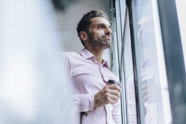 Thoughtful mature businessman with coffee cup looking through window - JOSEF16944