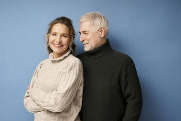 Happy woman with mature man standing against blue background - RSKF00028