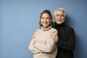Happy mature couple standing together against blue background - RSKF00029