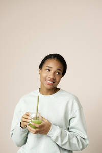 Kontemplative Frau mit grünem Smoothie vor einer Wand - RSKF00038