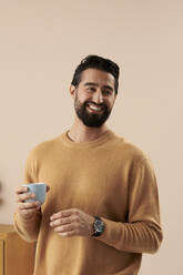 Glücklicher Mann mit Kaffeetasse vor einer Wand - RSKF00056