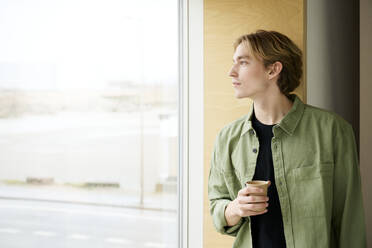 Nachdenklicher Mann schaut aus dem Fenster und hält eine Kaffeetasse - RSKF00059
