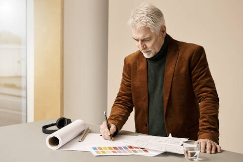 Ältere Modedesignerin skizziert auf Papier am Schreibtisch im Atelier - RSKF00069