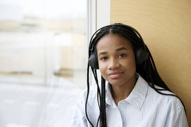 Smiling young woman with braided hair wearing wireless headphones - RSKF00081