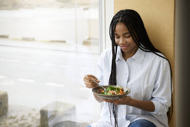Lächelnde Frau isst Salat am Fenster - RSKF00082