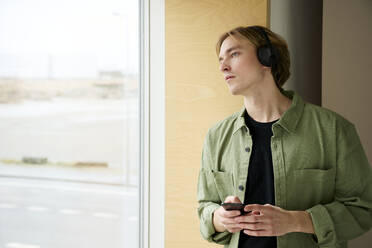 Nachdenklicher Mann, der aus dem Fenster schaut und ein Mobiltelefon hält - RSKF00083