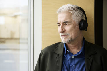 Smiling mature man listening to music through headphones - RSKF00091