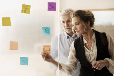 Businesswoman drawing on adhesive note by colleague at office - RSKF00106