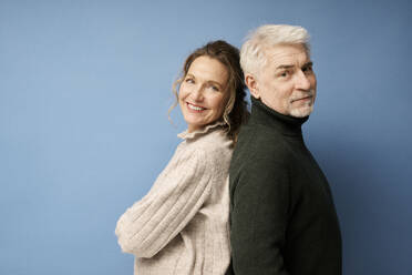 Älterer Mann und Frau stehen Rücken an Rücken vor blauem Hintergrund - RSKF00108