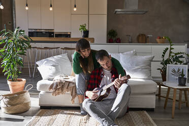 Girlfriend sitting by boyfriend playing guitar at home - VEGF06197