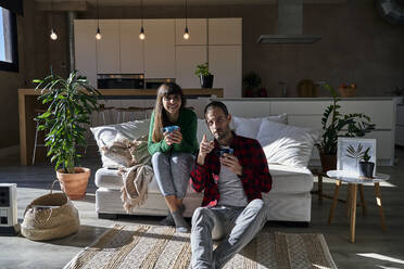 Couple enjoying drinks sitting in living room at home - VEGF06203