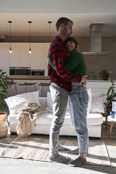 Man embracing girlfriend standing in living room at home - VEGF06207