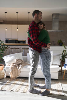 Mann umarmt Freundin stehend im Wohnzimmer zu Hause - VEGF06207