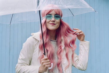 Smiling woman holding umbrella in front of wall - YTF00511