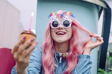 Glückliche Frau mit Scherzbrille und Muffin in der Hand genießt Geburtstag - YTF00512
