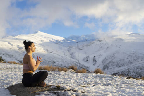 Frau in Gebetshaltung beim Yoga auf schneebedecktem Berg - LJF02476