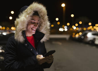 Glückliche Frau, die nachts mit ihrem Mobiltelefon im Internet surft - LJF02478