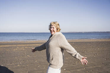 Glückliche ältere Frau mit ausgestreckten Armen beim Spaziergang am Strand - UUF28153