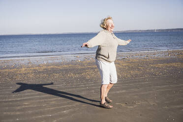 Glückliche ältere Frau genießt vor dem Meer an einem sonnigen Tag - UUF28156