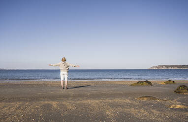 Senior woman with arms outstretched admiring sea at beach - UUF28159