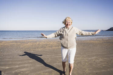 Glückliche sorglose ältere Frau mit ausgestreckten Armen tanzt am Strand - UUF28163