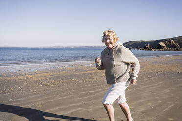 Glückliche ältere Frau, die am Strand am Meer läuft, an einem sonnigen Tag - UUF28169