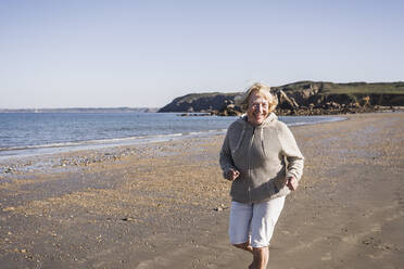 Glückliche ältere Frau läuft am Strand an einem sonnigen Tag - UUF28171