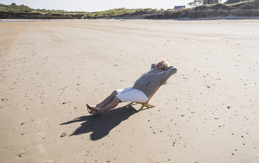 Ältere Frau entspannt sich auf einem Liegestuhl am Strand - UUF28174