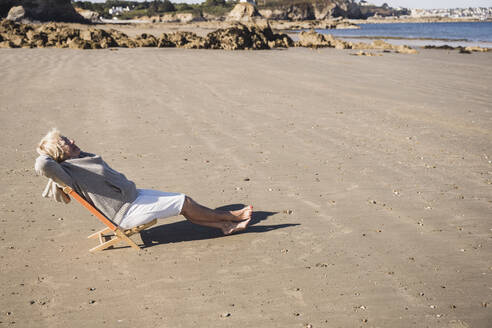 Ältere Frau entspannt sich am Strand an einem sonnigen Tag - UUF28175