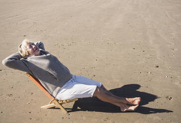 Senior woman with hands behind head relaxing at beach on sunny day - UUF28176