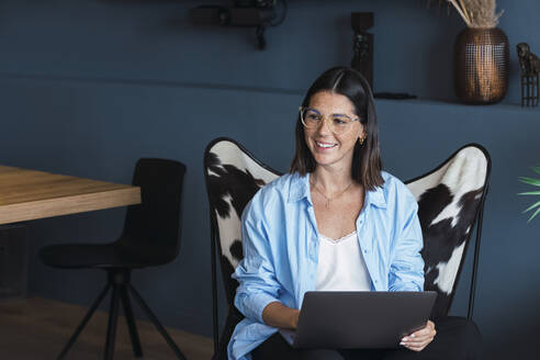 Lächelnde junge Geschäftsfrau mit Laptop zu Hause - PNAF05002