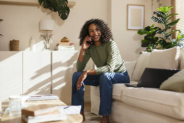 Smiling freelancer with curly hair sitting in home office - EBSF02722