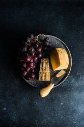 Von oben schwarzer Steinteller mit Käse und rohen leckeren Trauben auf dunklem Betontisch - ADSF43118