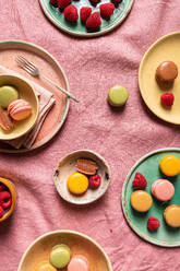 Draufsicht auf sortierte runde Teller mit verschiedenen süßen bunten französischen Makronen und Beeren auf rosa Tischtuch - ADSF43131