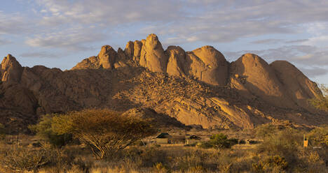 Malerischer Blick auf felsige Berge mit trockenem Gras unter bewölktem Himmel an einem sonnigen Tag in Namibia - ADSF43160