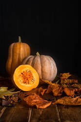 Zusammensetzung der reifen orange Kürbisse und trockenen Herbst Ahornblätter auf Holztisch in der Nähe von schwarzen Wand platziert - ADSF43168