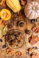 Top view Zusammensetzung von appetitlichen Muffins mit Schokolade-Chips auf Holztisch unter verstreuten Herbstblätter und Kürbisse platziert gemacht - ADSF43169