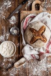 Top view of messy wooden rustic table in wheat flour and board with freshly baked sourdough bread loaf - ADSF43173