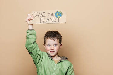 Junge demonstriert Karton Plakat mit Save the Planet Inschrift und Hand gezeichnet Erde gegen beige Hintergrund - ADSF43192