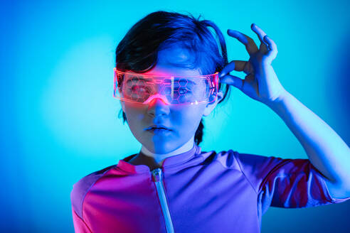 Kleines futuristisches Mädchen mit VR-Brille erkundet den Cyberspace und interagiert mit der virtuellen Welt in einem dunklen, von blauem Neonlicht beleuchteten Raum - ADSF43195