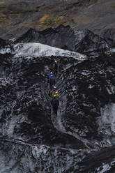 Von oben: unkenntliche Touristen in Oberbekleidung und Schutzhelmen beim Trekking auf dem Solheimajokull-Gletscher in Island - ADSF43199