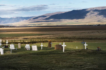 Picturesque landscape of catholic cemetery with white tombstones placed on grassy lawn under cloudy blue sky in Iceland - ADSF43215