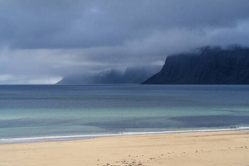Atemberaubende Landschaft mit wogendem Meer, felsigen Bergen und sandiger Küste unter schweren Wolken in Island - ADSF43217