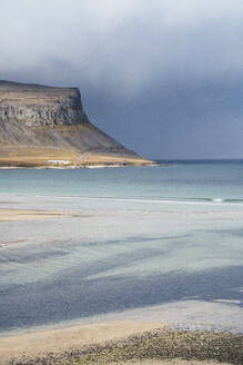 Atemberaubende Landschaft mit wogendem Meer, felsigen Bergen und sandiger Küste unter schweren Wolken in Island - ADSF43218