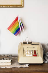 Vintage-Telefon mit LGBT-Flagge auf Holztisch in der Nähe Bücher gegen weiße Wand platziert - ADSF43220