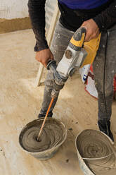 Abgeschnittener, nicht erkennbarer Mann in schmutziger Kleidung, der einen Handmixer benutzt, um Zement für eine Wand während Renovierungsarbeiten vorzubereiten - ADSF43231