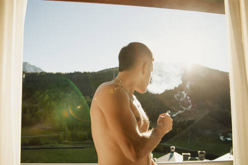 Hemdloser Mann raucht einen Marihuana-Joint auf der Terrasse am Morgen - CAVF96578