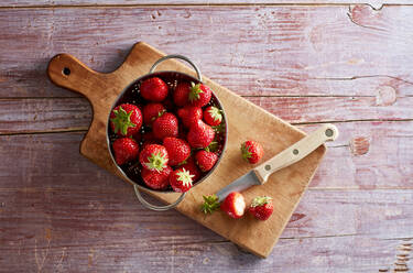 Colander with fresh strawberries lying on cutting board - KSWF02267