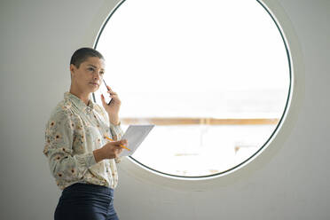 Geschäftsfrau mit Buch in der Hand, die in der Nähe des Fensters mit einem Mobiltelefon spricht - FBAF02015