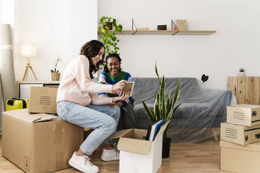 Young woman with friend looking at photo frame in living room at home - JCZF01168